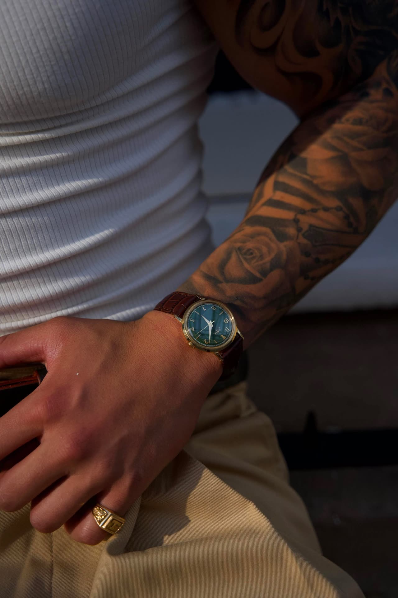 A gold watch and signet ring against a white ribbed vest