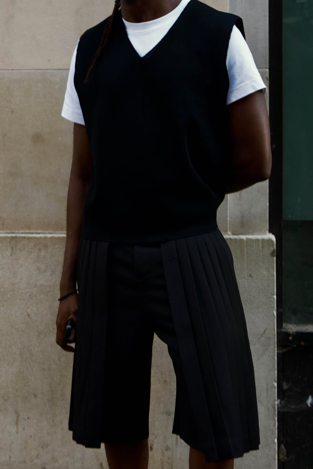 A complete look: knitted vest, white tee and pleated tailored shorts, photographed on the street
